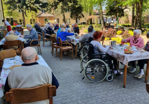 Mieszkańcy siedzący przy stołach na zewnątrz w trakcie grilla, w tle widoczny nasz ogród.