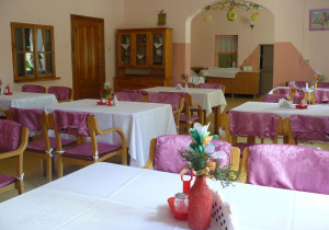 zdjęcie jadalni, na którym widnieją stoły z białymi obrusami i krzesła z różowymi obszyciami. Na stołach stoją wazony z kwiatami